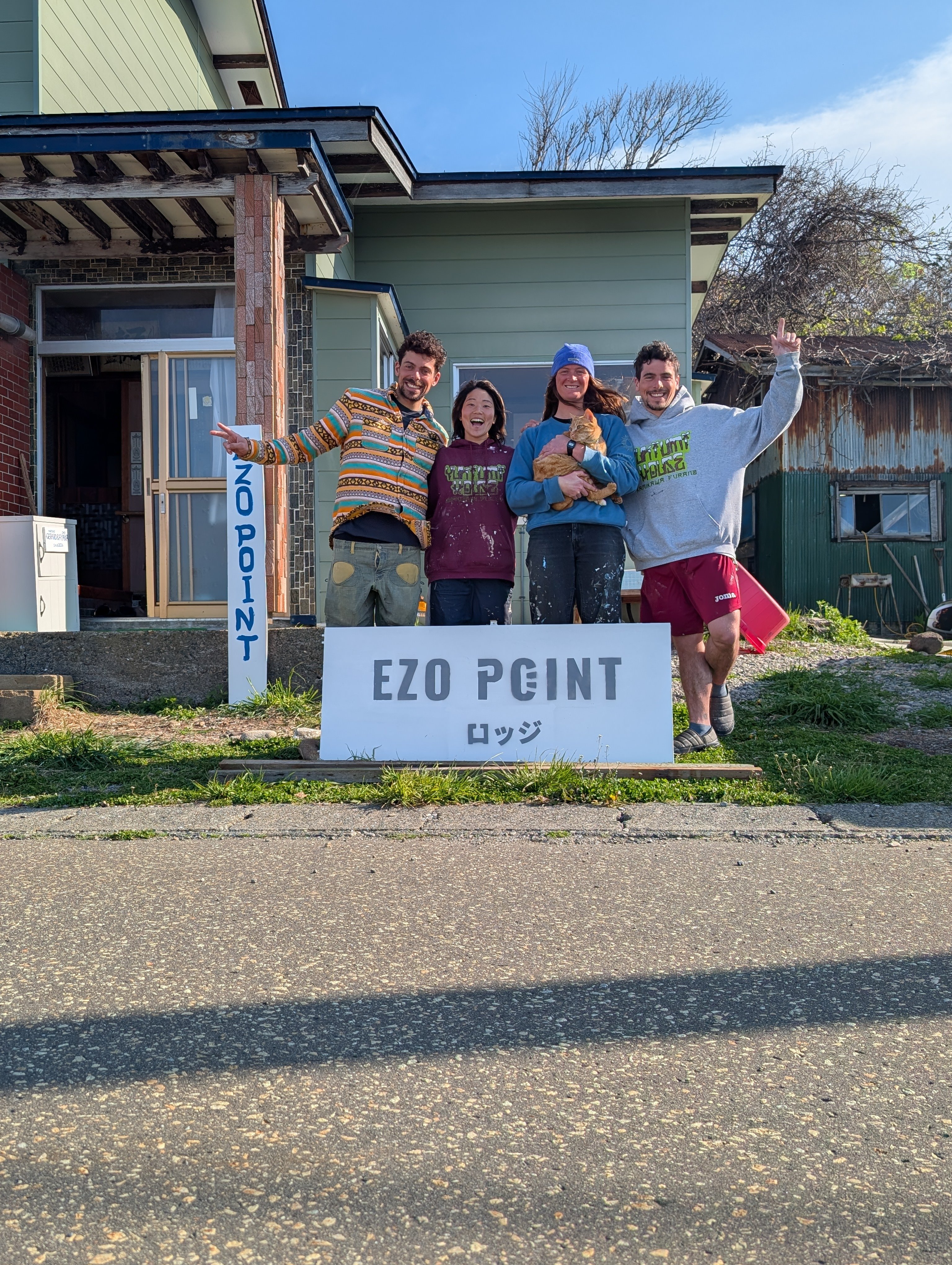 EZO POINT のロッジ看板の前で、キロちゃんを抱える Ayaka、Gerard と仲間たち
