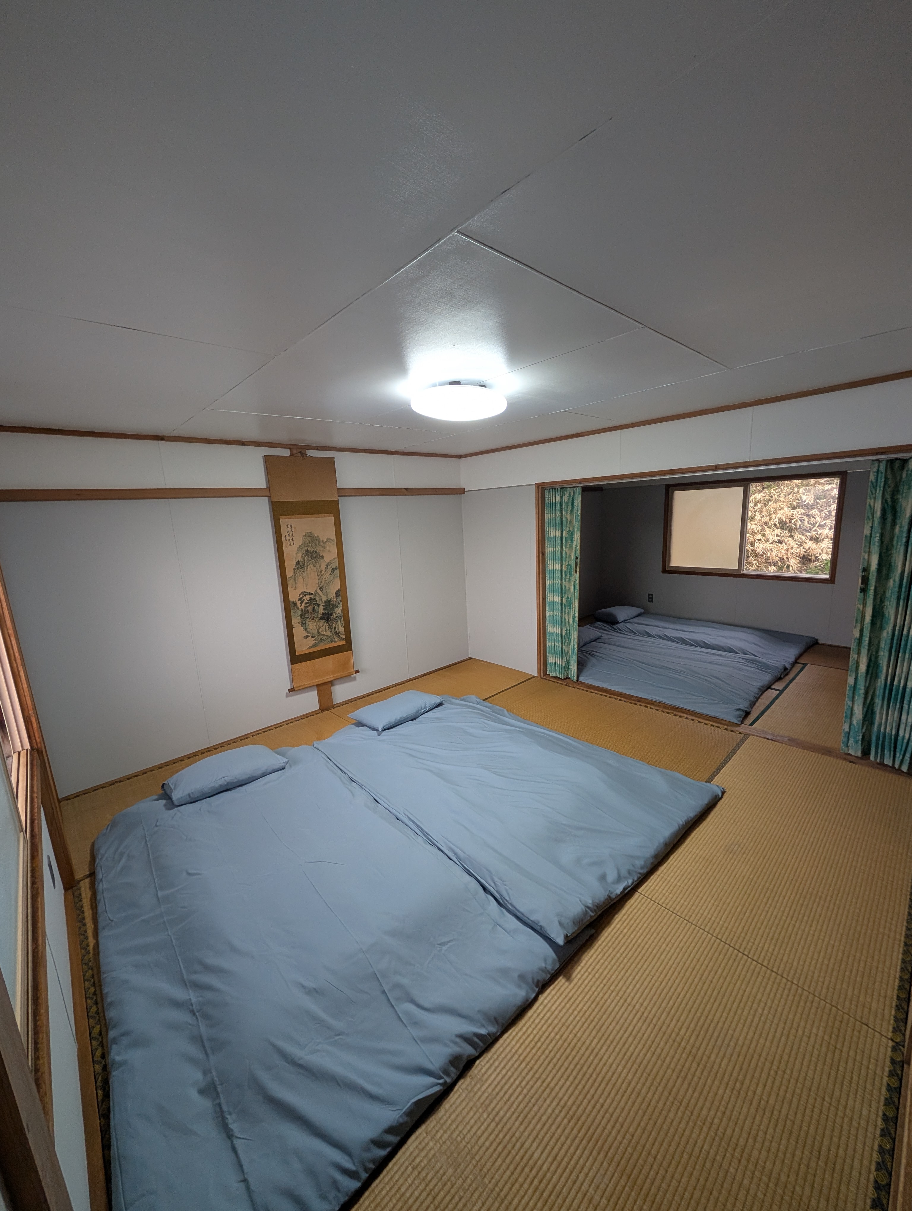 複数の布団が敷かれ、壁に掛け軸が下がる広い続き間の畳の部屋。